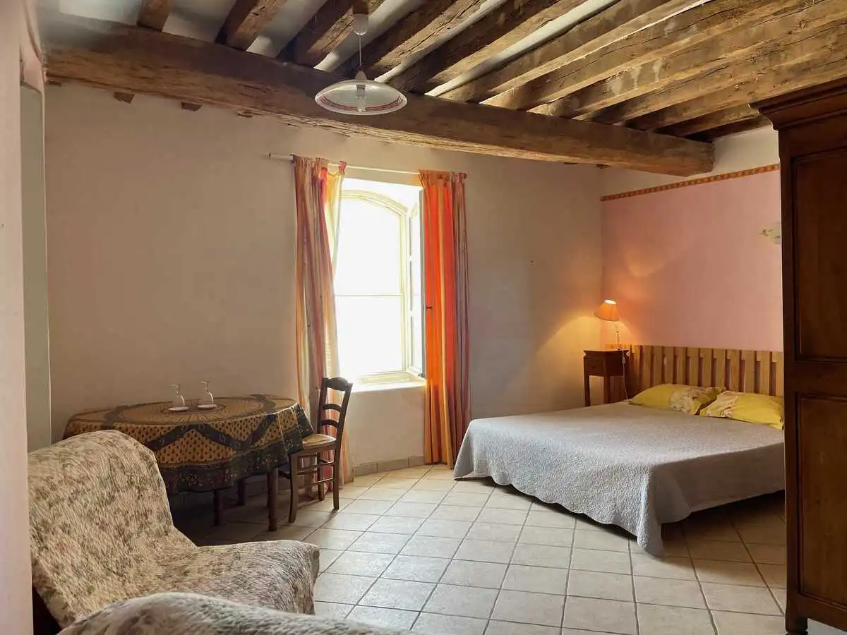 Chambre d'hôtes spacieuse avec lit double et coin repas au Château de la Gabelle en Drôme provençale, décorée dans un style rustique avec poutres apparentes.
